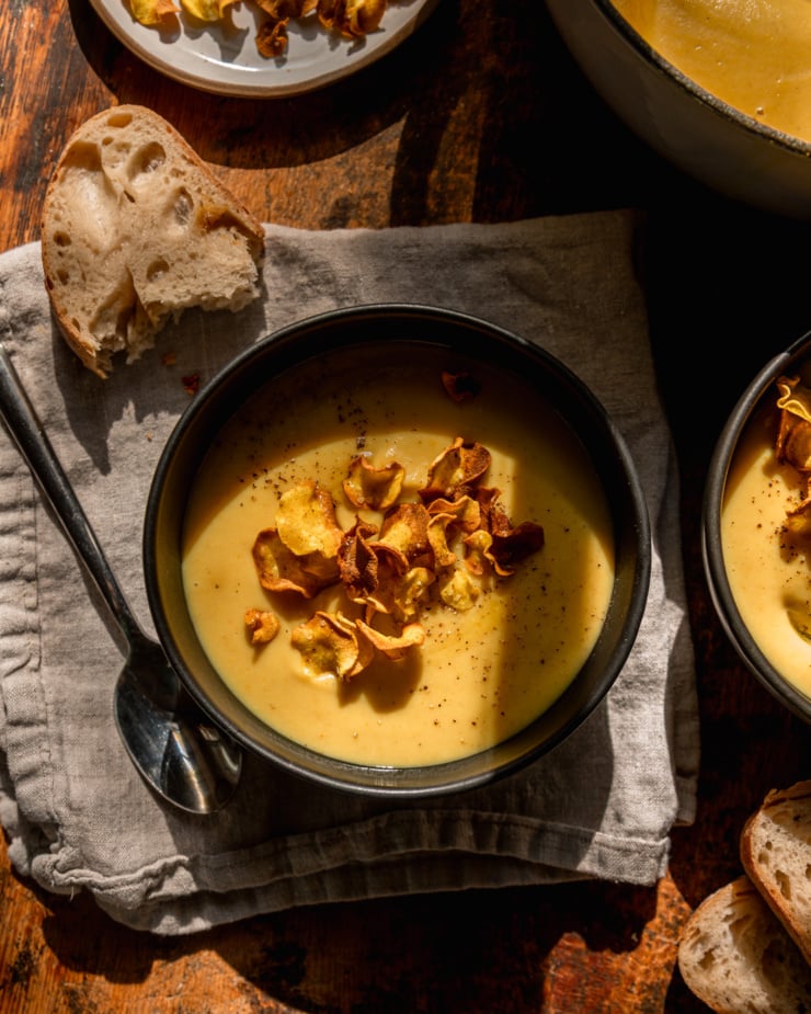 The overhead photo shows an individual parsnip soup, garnished with parsnip slices. The bread is nearby and the photo was taken in direct sunlight.