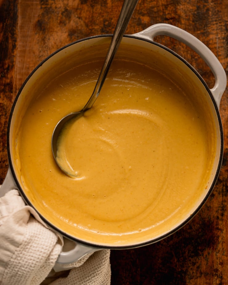 An overhead view shows a Dutch oven filled with creamy pureed parsnip soup. A ladle sticks out of the pot.