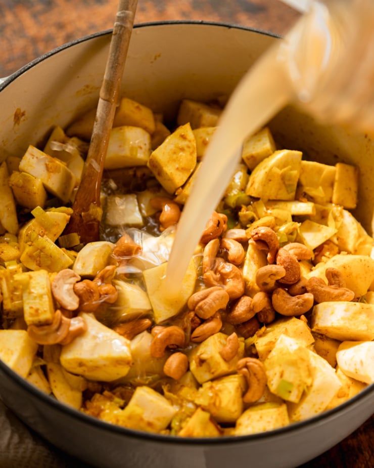 3/4 angle shot shows vegetable stock poured over cooked vegetables and roasted cashews in a pot.