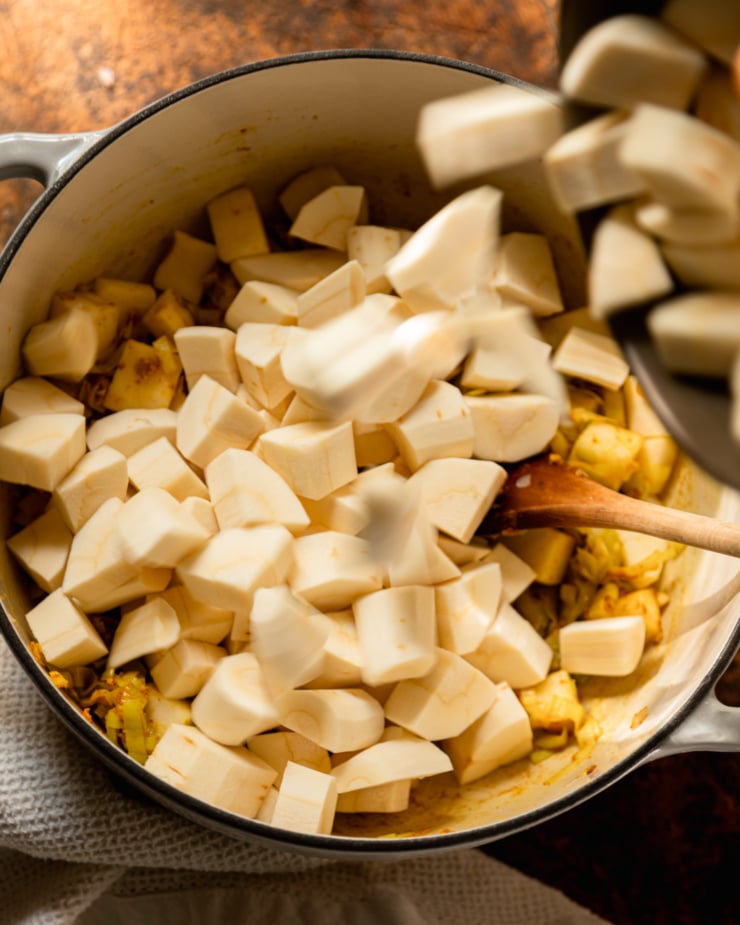 An overhead shot shows chopped parsnips being poured into a large Dutch oven pot.