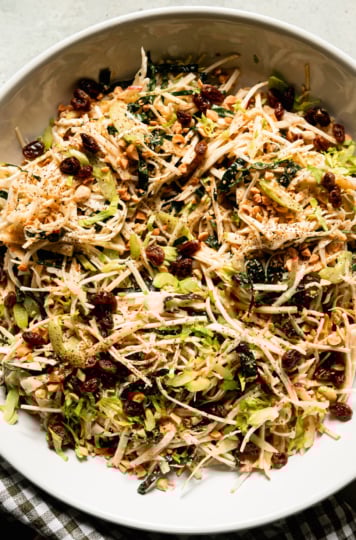 An up close, overhead shot shows a celery root salad in a wide bowl. The salad also features celery, kale, cabbage, apples, peanuts and raisins. All of the fruit and vegetables are julienned fine.