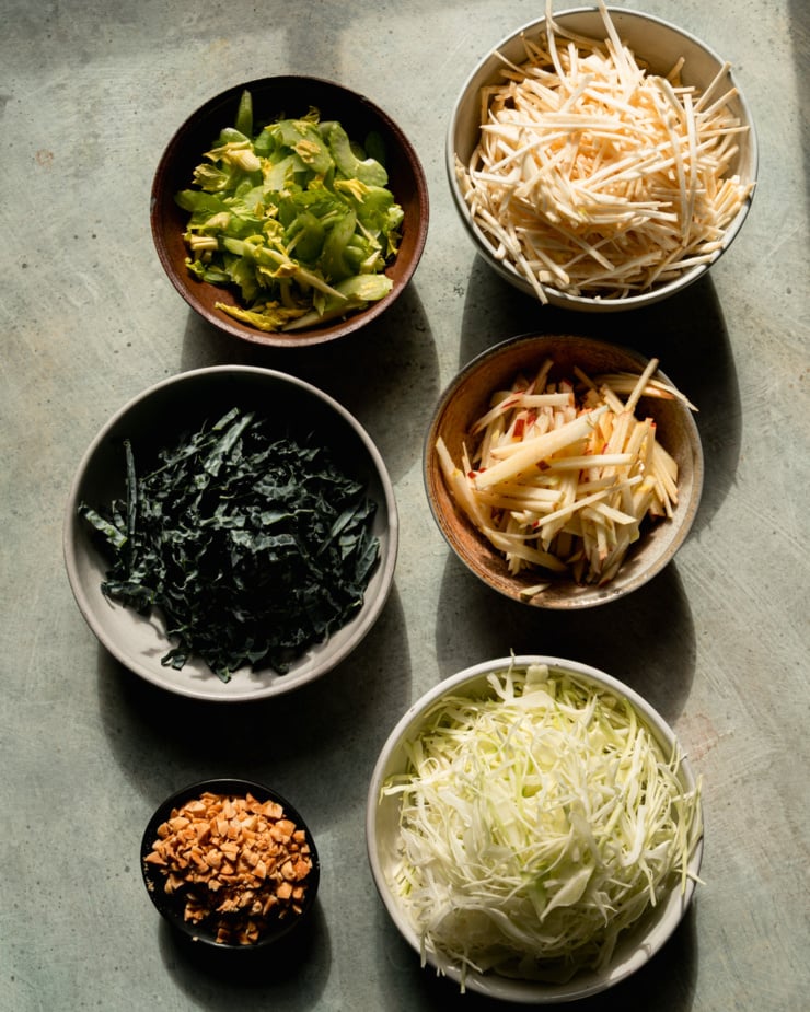 The overhead photo shows the bowl filled with julienned celery root, julienned apples, chopped cabbage, chopped peanuts, sliced ​​kale and sliced ​​celery.