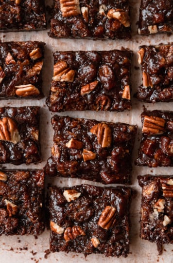 An overhead shot shows gooey chocolate pecan bars on top of parchment paper.
