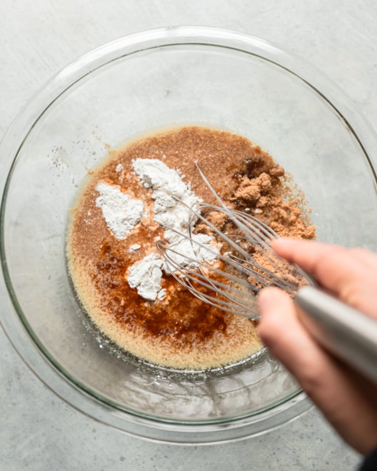 The overhead photo shows a hand holding a mixer in a bowl. Bowl with brown sugar, melted vegan butter, flax