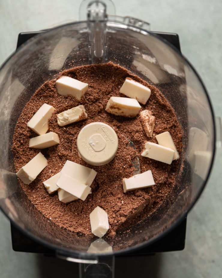 The overhead photo shows the cocoa and dry flour mixture in the food processor with some cold vegan butter on top.