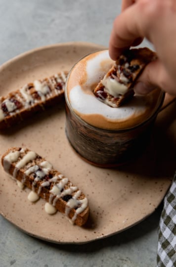 A 3/4 angle image shows a hand dunking a biscotti into a frothy coffee.