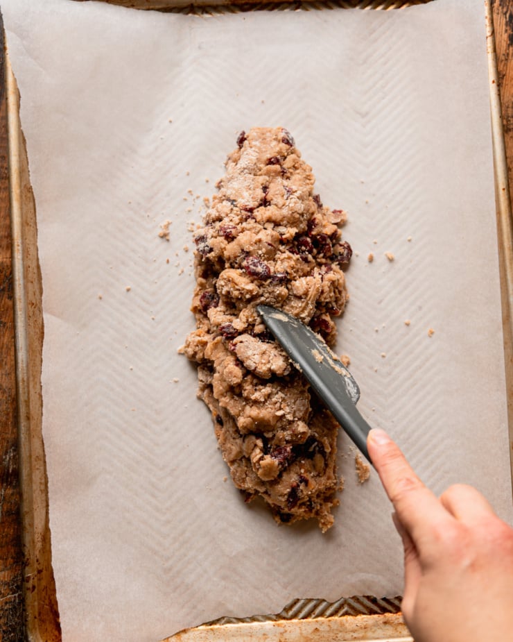 The top-down photo shows a hand using a spatula to transfer cookie dough to a baking sheet.