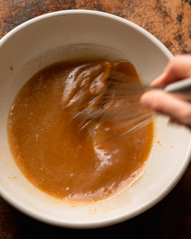 Top-down photo shows a hand using a whisk to put some liquid ingredients into a bowl.