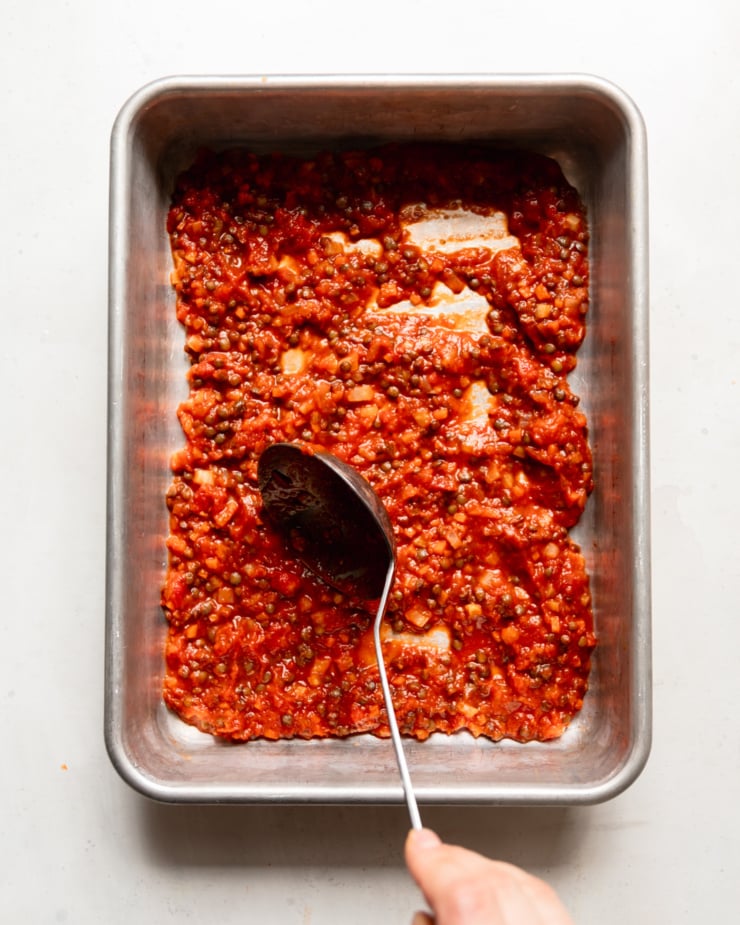 The overhead photo shows a hand spooning lentil and vegetable marinade mixture into a baking dish.