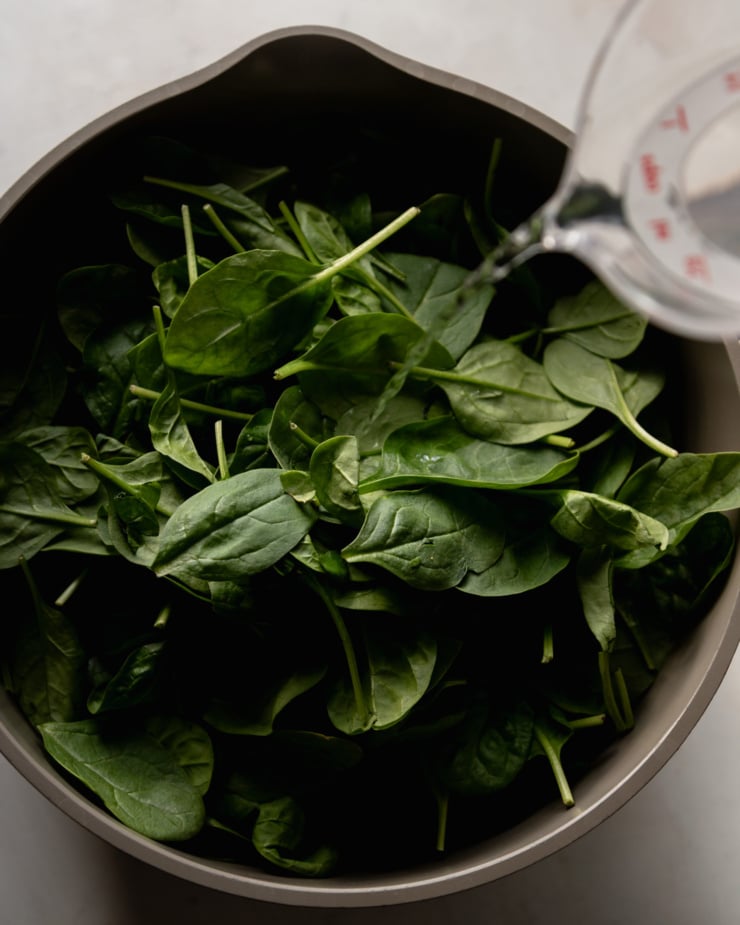 The top view shows a pot filled with baby spinach. The measuring cup is pouring water into the pot.