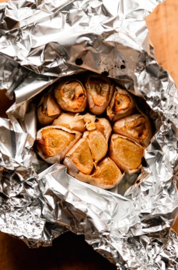 An overhead shot shows a foil-wrapped head of garlic that has been roasted. The cloves are exposed and golden.
