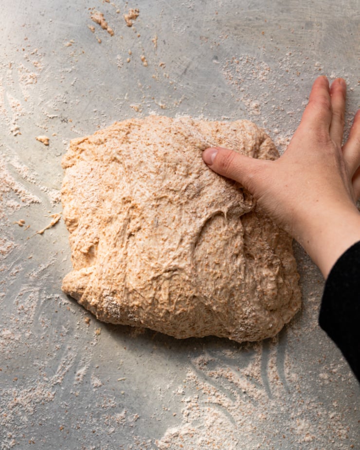 An overhead shot shows a hand folding a piece of dough over with lots of flour dusted everywhere.