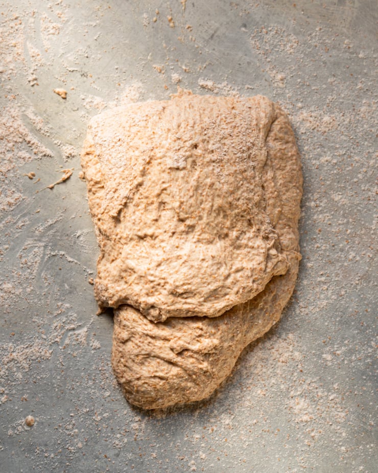 An overhead shot shows a piece of bread dough that has been folded in half with dustings of flour.