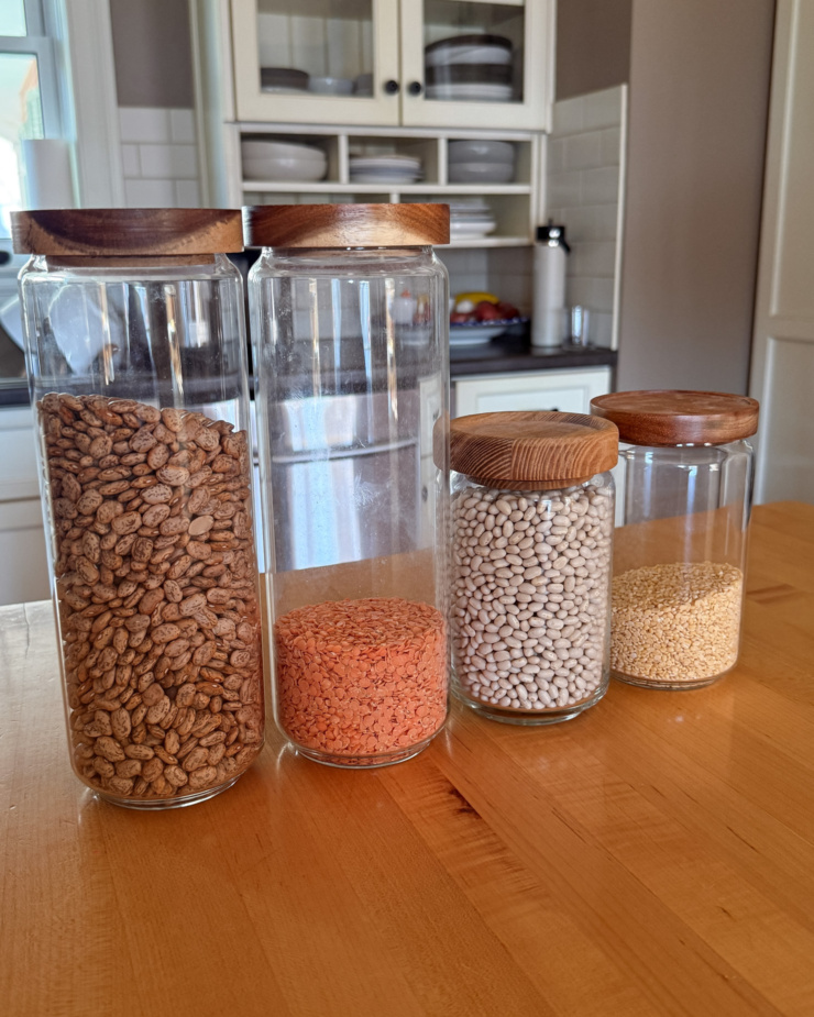 A head-on shot shows glass jars with beans and lentils with kitchen cupboards in the background.