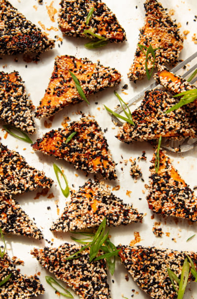 An overhead shot shows baked sesame tofu triangles garnished with sliced green onions.