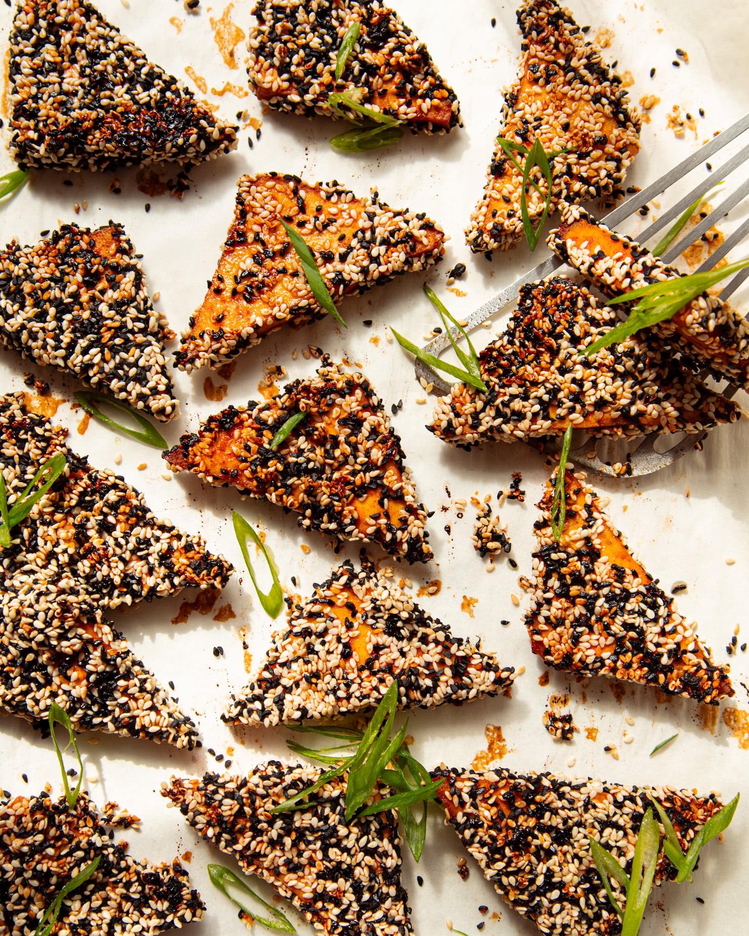 An overhead shot shows baked sesame tofu triangles garnished with sliced green onions.