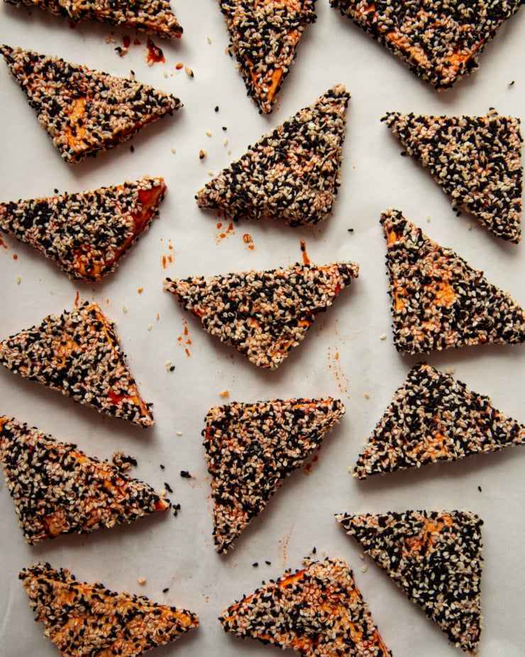 An overhead shot shows triangular cuts of tofu coated in a red saucy mixture and sesame seeds.