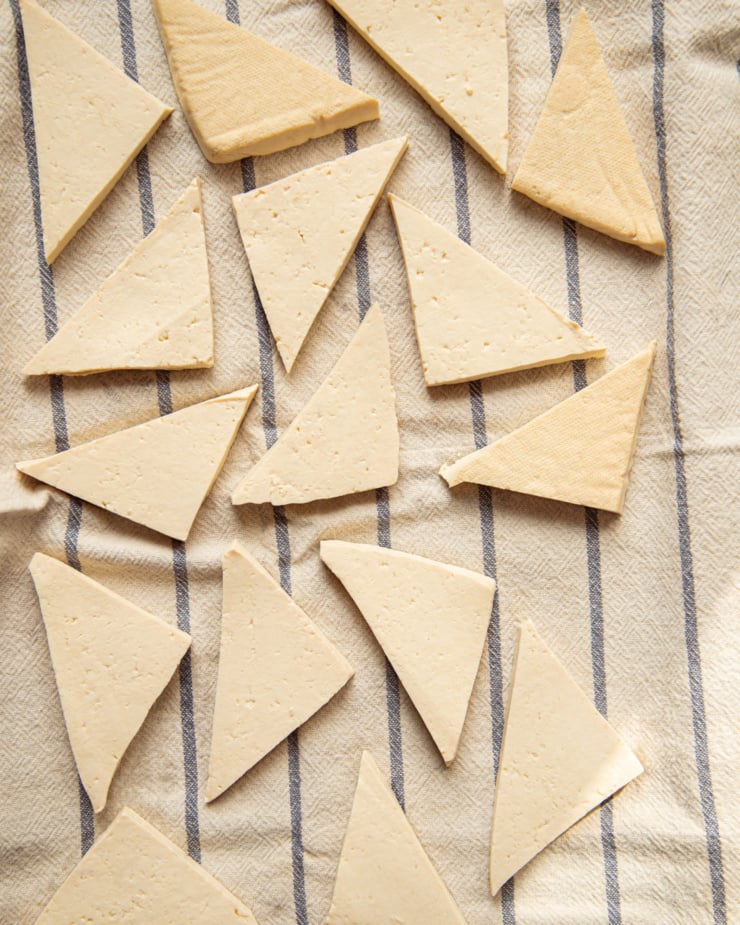 An overhead shot shows thin tofu triangles arranged on a clean kitchen towel.