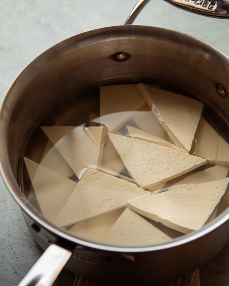 A 3/4 angle shot shows a saucepan with water and a bunch of tofu triangles floating in it.