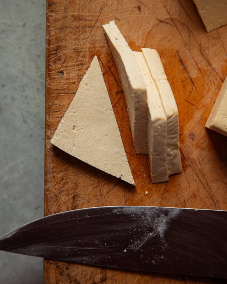 An overhead shot shows a piece of tofu cut into little triangular slices. A knife is nearby.