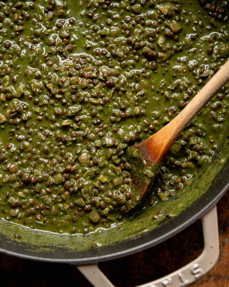 An overhead, up close shot shows spinach and coconut stewed lentils in a pot. A wooden spoon is sticking out of the lentils.