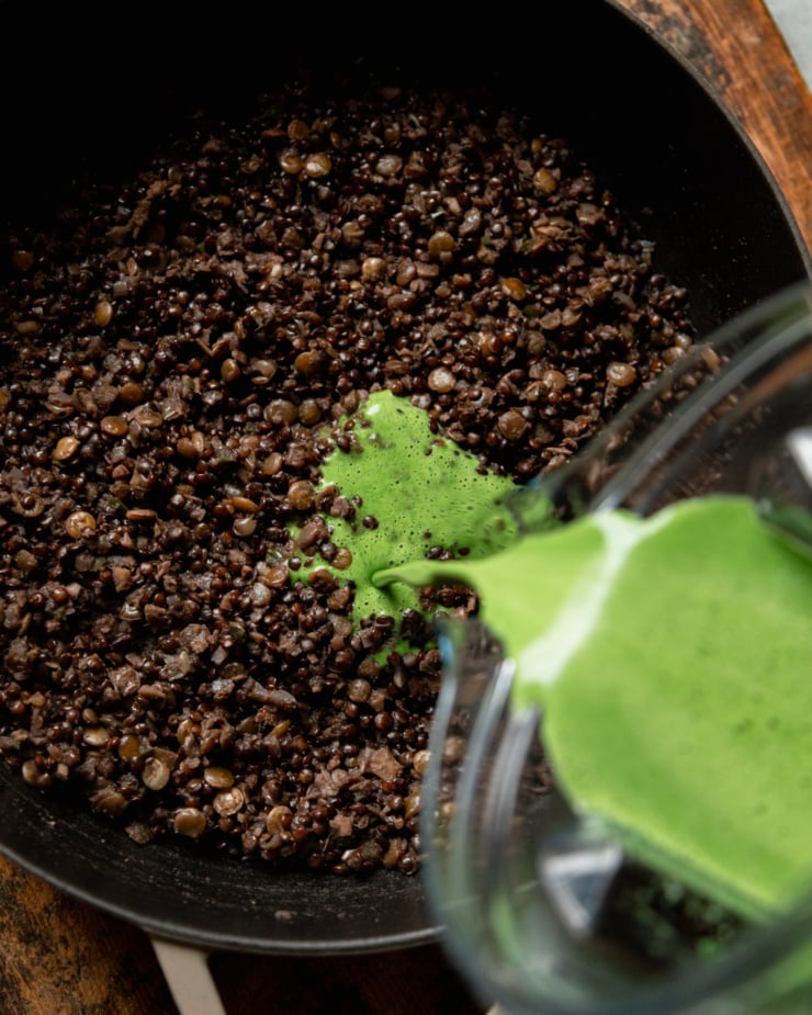 An overhead shot shows a green, creamy coconut milk blend being poured into a pot of lentils.