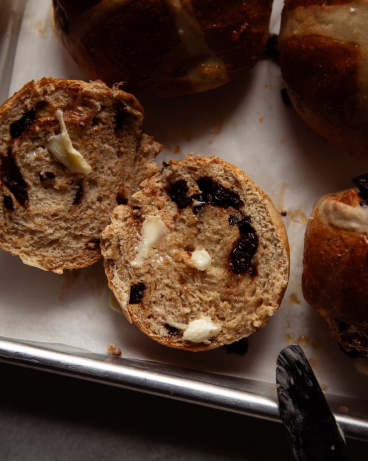 An overhead shot shows a split vegan hot cross bun with bits of vegan butter melting into the crevices.
