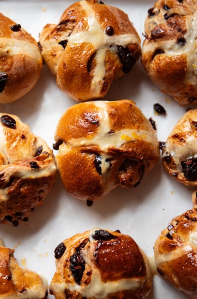 An overhead shot shows freshly baked and glazed vegan hot cross buns with dried cherries and chocolate.