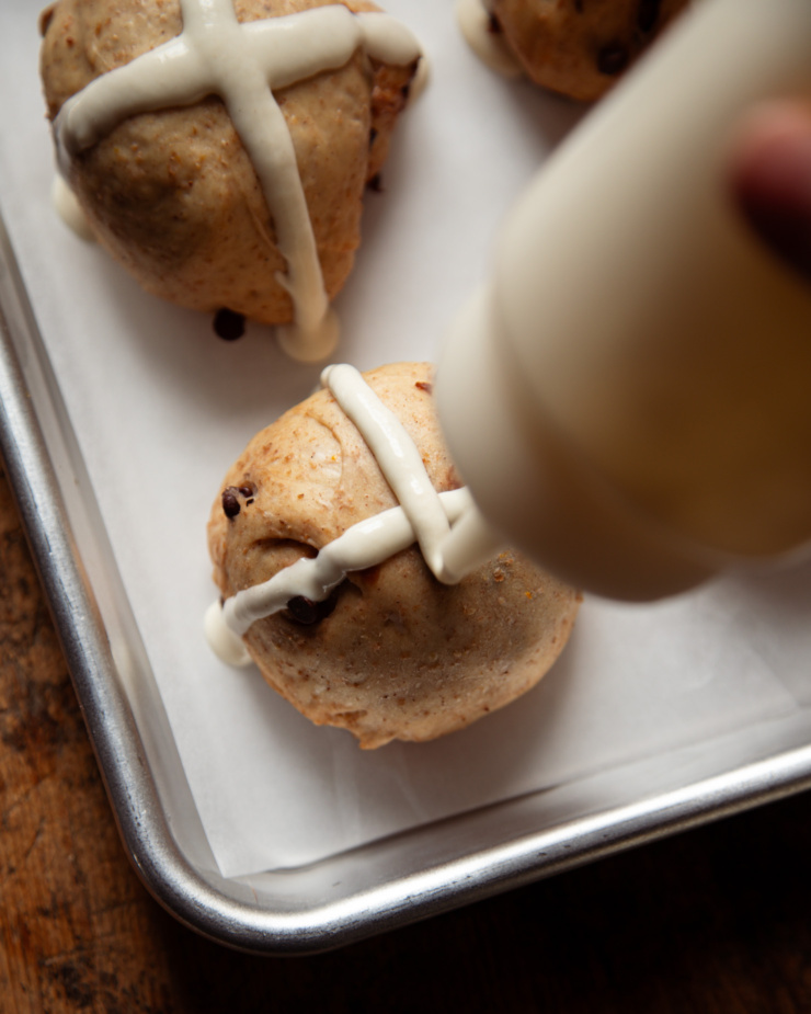 An overhead shot shows the flour mixture being piped into crosses on top of hot cross buns.