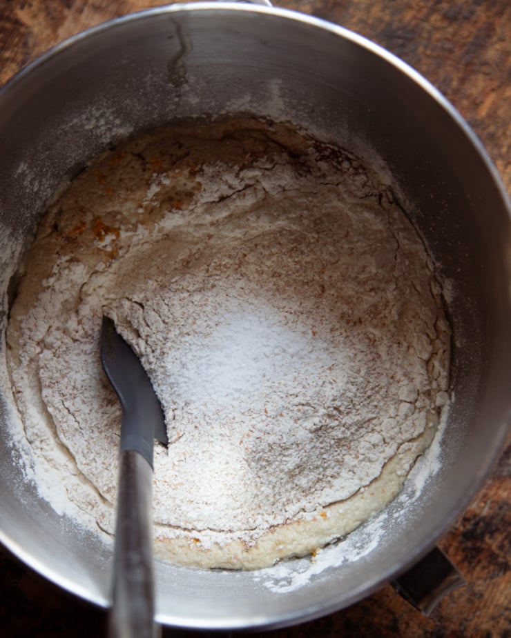 An overhead shot shows dry ingredients added to wet ones in a mixing bowl. A spatula is in the bowl also.