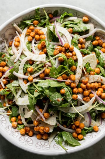 An overhead shot shows a chickpea arugula salad in a bowl with shaved fennel and red onion. The chickpeas are crispy and browned.
