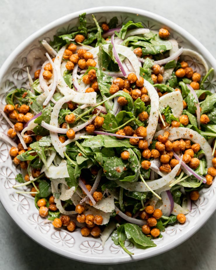 An overhead shot shows a chickpea arugula salad in a bowl with shaved fennel and red onion. The chickpeas are crispy and browned.