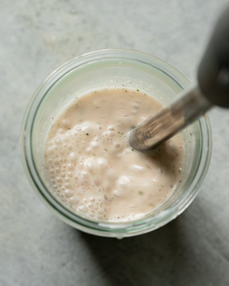An overhead shot shows an immersion blender mixing up a salad dressing in a jar.