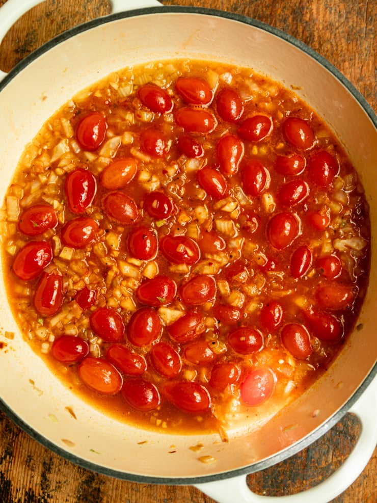 Overhead shot of a Dutch oven filled with cherry tomatoes simmering in a spiced harissa broth with diced fennel and shallots.