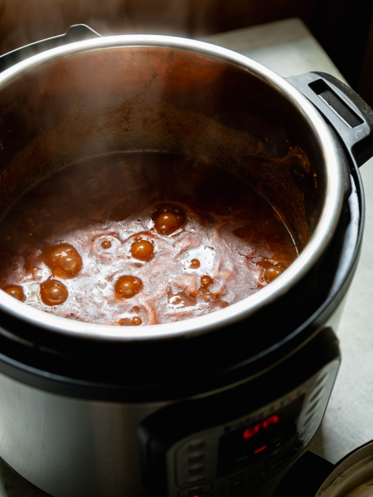 Close-up of the bean cooking liquid bubbling and steaming inside the Instant Pot insert before the beans are stirred in.