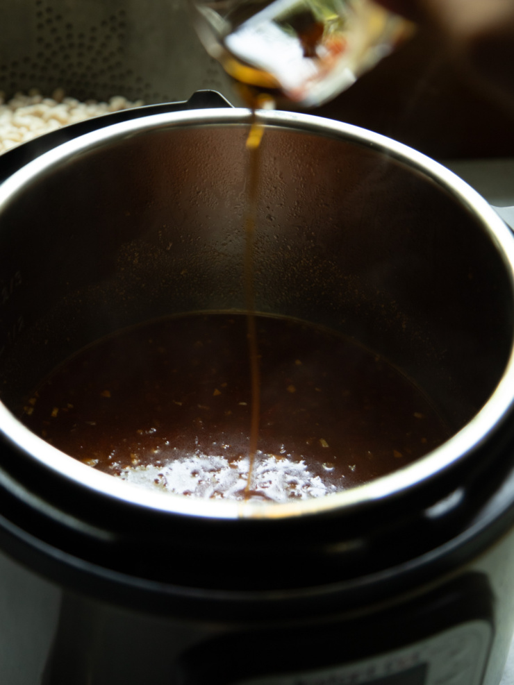 Close-up of maple syrup streaming from its container into the simmering sauce base in the Instant Pot.
