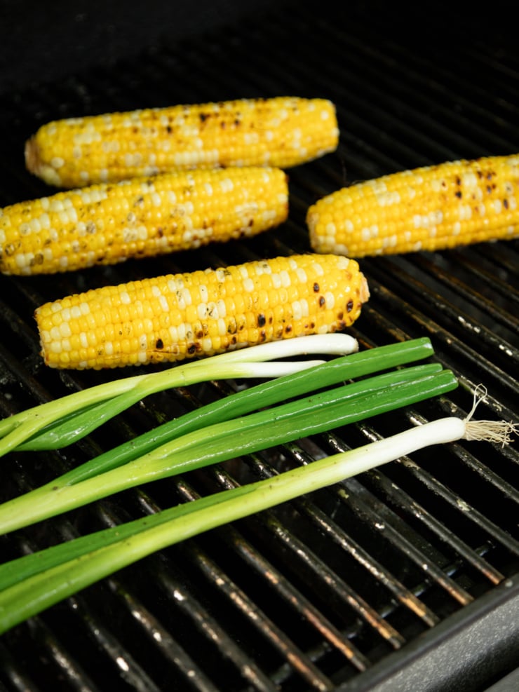 Charred corn on the cob and green onions cooking on a grill grate.