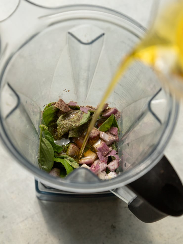 Basil leaves, chopped shallot, and olive oil being poured into a blender to make basil lime dressing.