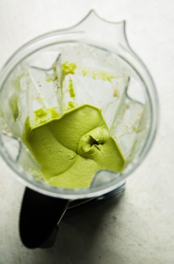 Overhead view of a blender jar with smooth, whipped garlic white bean dip left inside after blending, blade visible at the bottom.