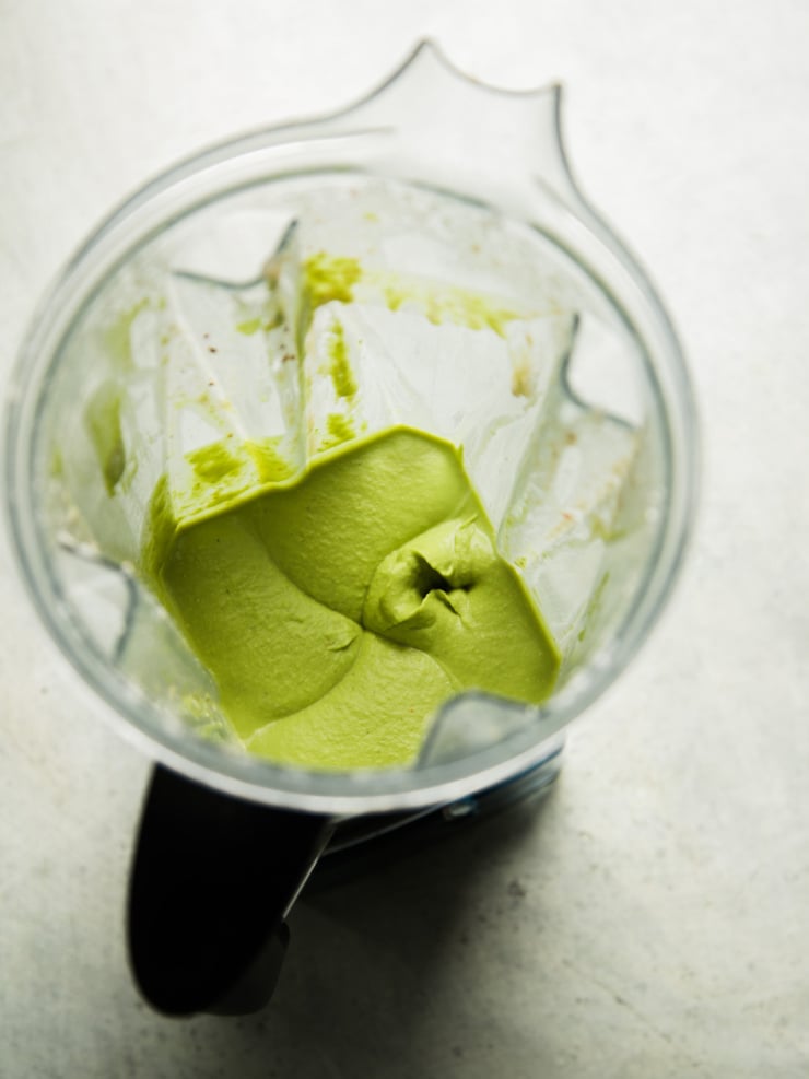Overhead view of a blender jar with smooth, whipped garlic white bean dip left inside after blending, blade visible at the bottom.