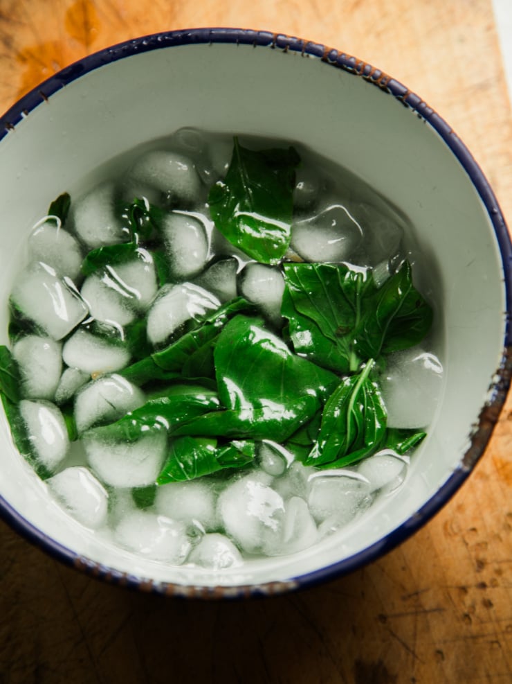 Fresh basil leaves in an ice bath for blanching, part of the process for making this garlic white bean dip.