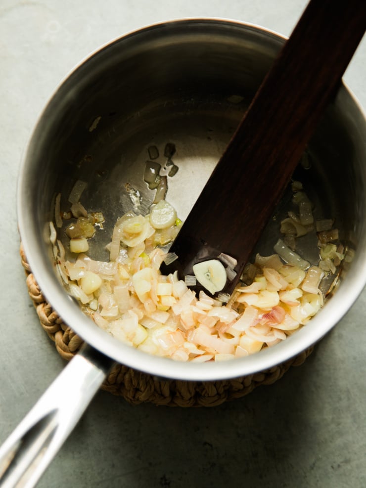 Chopped shallot and garlic softening in a saucepan, an early step in this garlic white bean dip recipe.