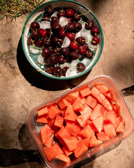 Overhead image shows a bowl of fresh cherries on ice next to a container of cubed watermelon.