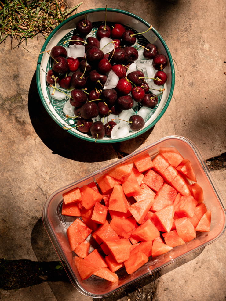 Overhead image shows a bowl of fresh cherries on ice next to a container of cubed watermelon.
