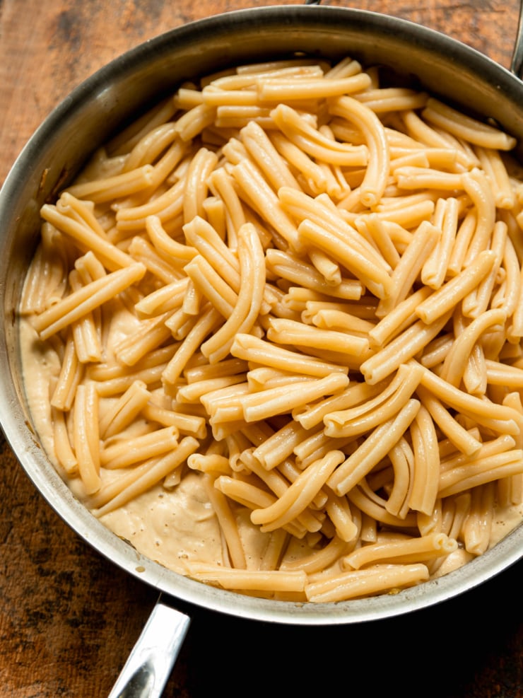 Cooked casarecce pasta piled on top of a creamy sauce in a stainless steel skillet, before being tossed together.
