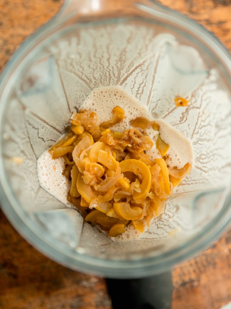 Overhead view of caramelized onions and squash added to a creamy blended sauce in a blender jar.