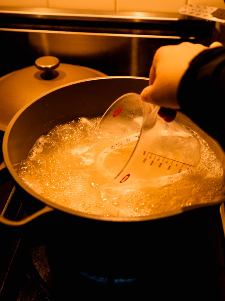 Hot pasta cooking water being scooped up with a measuring cup from a large pot on the stove.