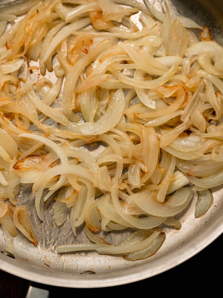 Close-up of slightly golden caramelized onions in a stainless steel skillet.