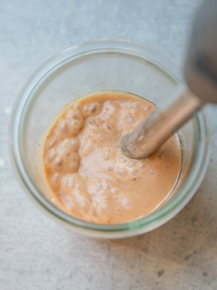 Close-up overhead view of a small glass jar of emulsified red wine vinegar dressing being mixed with an immersion blender.
