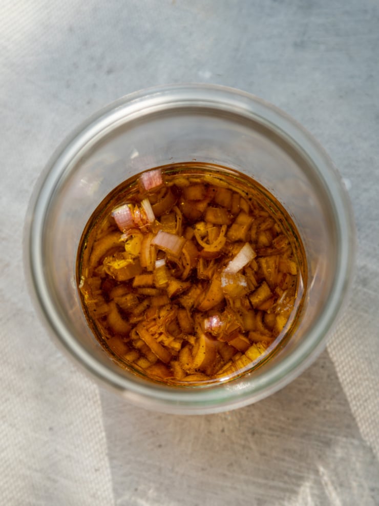 Overhead close-up of diced shallots steeping in an amber-colored dressing inside a glass jar.